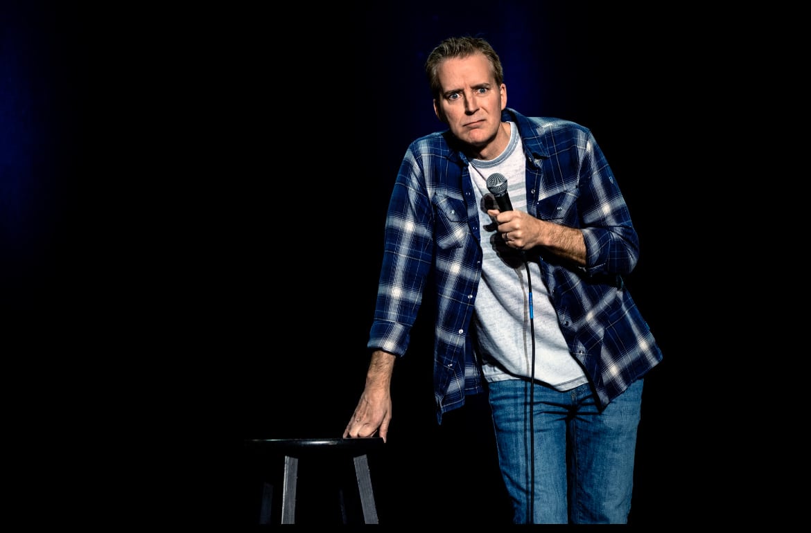 A comedian performing solo on stage in front of a black background